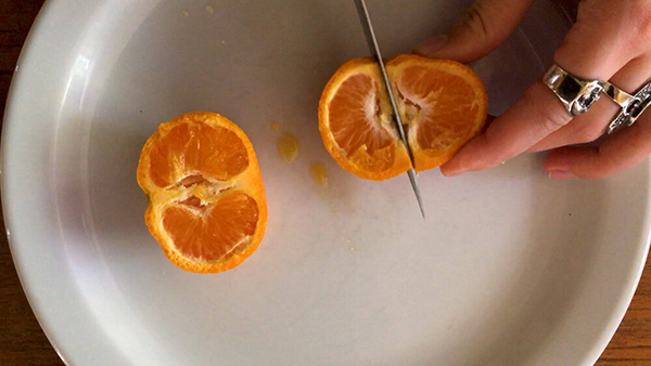 white hands cutting an orange with a knife